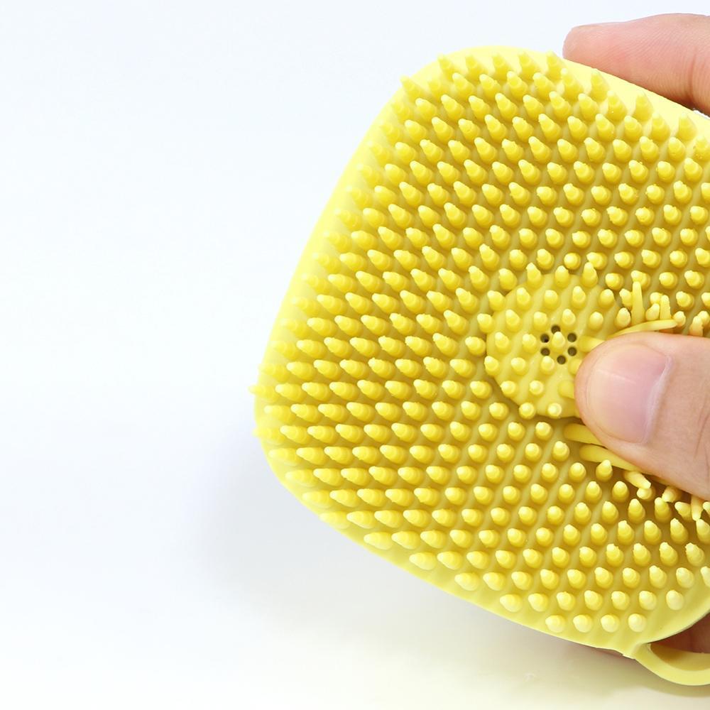 Yellow silicone body bath brush with dense textured bristle surface held in hand
