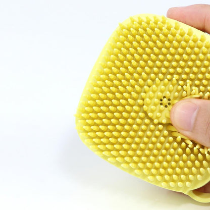 Yellow silicone body bath brush with dense textured bristle surface held in hand