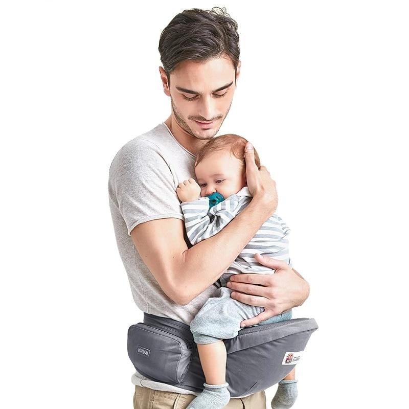 Padded hip seat baby carrier on adult waist, holding baby in front.